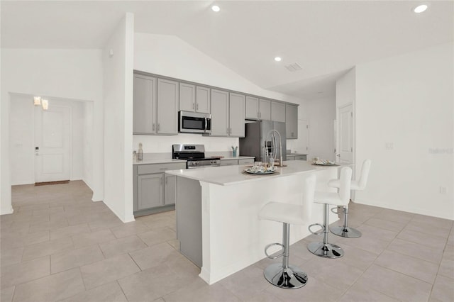 kitchen featuring gray cabinetry, vaulted ceiling, an island with sink, a kitchen bar, and stainless steel appliances