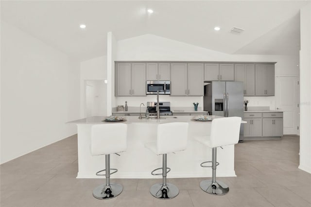 kitchen featuring gray cabinetry, lofted ceiling, an island with sink, and appliances with stainless steel finishes