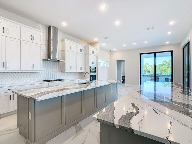 kitchen featuring wall chimney exhaust hood, a large island, light stone counters, and white cabinets