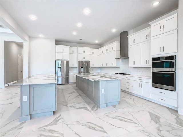 kitchen featuring an island with sink, wall chimney exhaust hood, stainless steel appliances, and white cabinetry