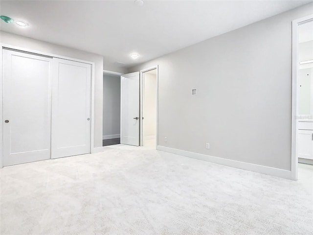 unfurnished bedroom with light carpet, a closet, and ensuite bath