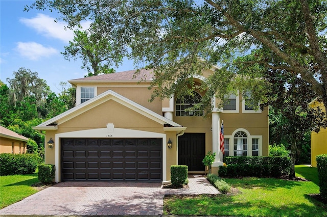 view of front of property featuring a front yard, decorative driveway, a garage, and stucco siding