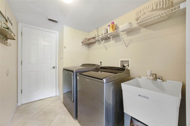 clothes washing area featuring light tile patterned floors, a textured ceiling, independent washer and dryer, and sink