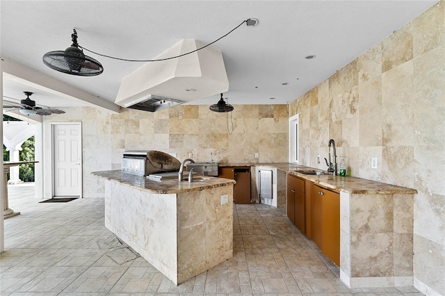 kitchen with light stone countertops, tile walls, kitchen peninsula, and sink