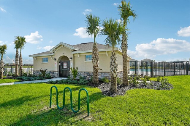 view of front of property featuring a front yard, fence, stucco siding, a community pool, and stone siding