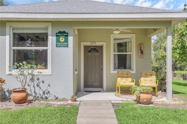 entrance to property featuring stucco siding, a shingled roof, and ceiling fan