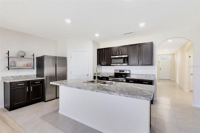 kitchen with a textured ceiling, a center island with sink, appliances with stainless steel finishes, sink, and light tile patterned flooring