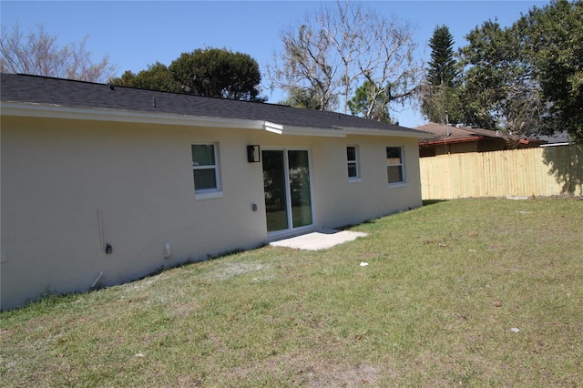 rear view of property with a yard, fence, and stucco siding