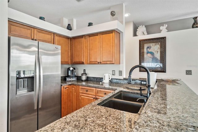 kitchen with dark stone counters, a textured ceiling, stainless steel fridge with ice dispenser, and sink