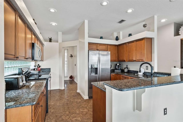 kitchen with dark stone countertops, a textured ceiling, stainless steel appliances, and kitchen peninsula