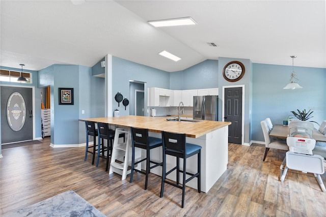 kitchen featuring sink, decorative light fixtures, stainless steel fridge with ice dispenser, white cabinetry, and butcher block counters