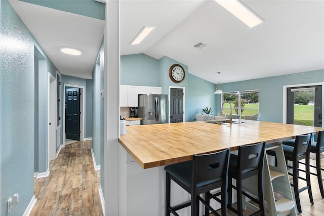 kitchen featuring a kitchen bar, stainless steel fridge, wooden counters, vaulted ceiling, and white cabinetry