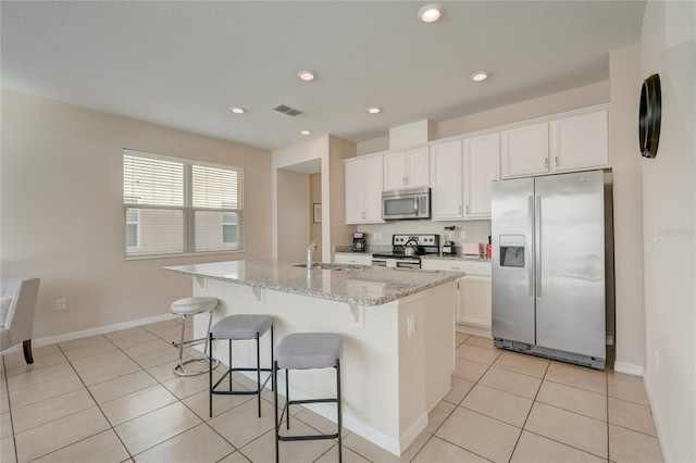 kitchen featuring appliances with stainless steel finishes, a kitchen island with sink, sink, light stone counters, and white cabinets