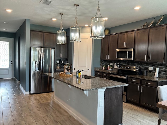 kitchen featuring a center island with sink, sink, appliances with stainless steel finishes, decorative light fixtures, and light hardwood / wood-style flooring