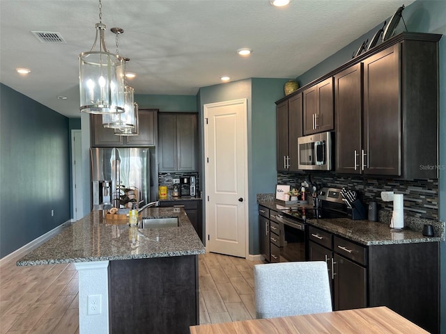 kitchen with appliances with stainless steel finishes, dark brown cabinets, sink, light hardwood / wood-style floors, and a kitchen island with sink