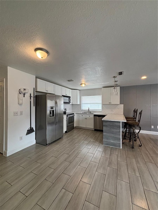 kitchen with white cabinets, appliances with stainless steel finishes, light hardwood / wood-style floors, and a textured ceiling