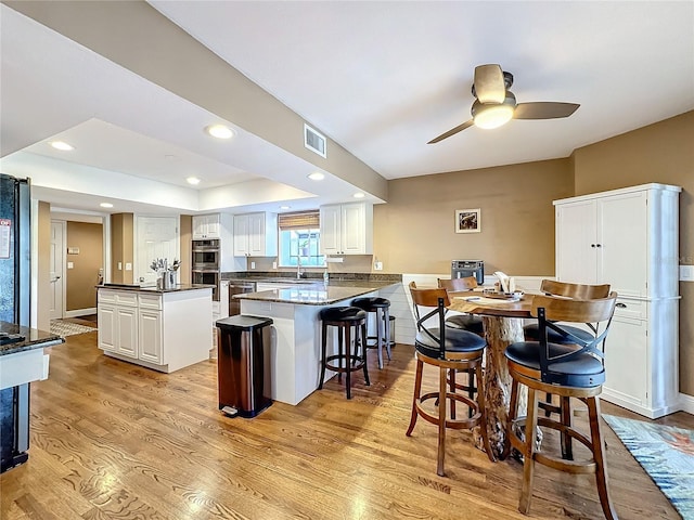 kitchen featuring double oven, light wood-type flooring, kitchen peninsula, and white cabinetry