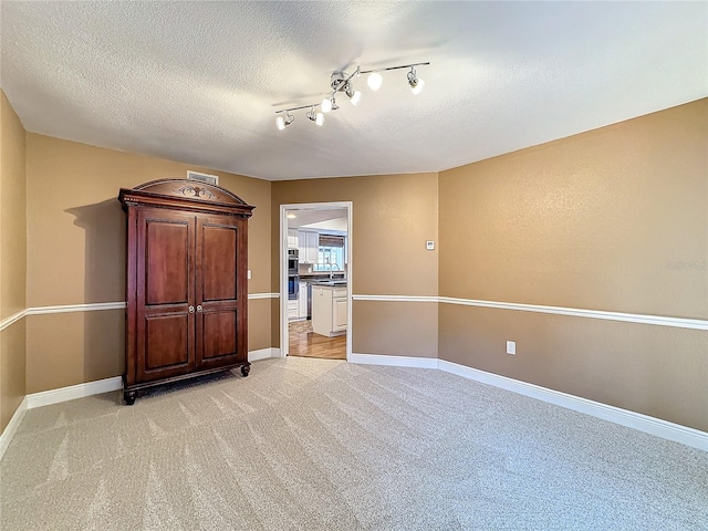 carpeted empty room featuring a textured ceiling and rail lighting