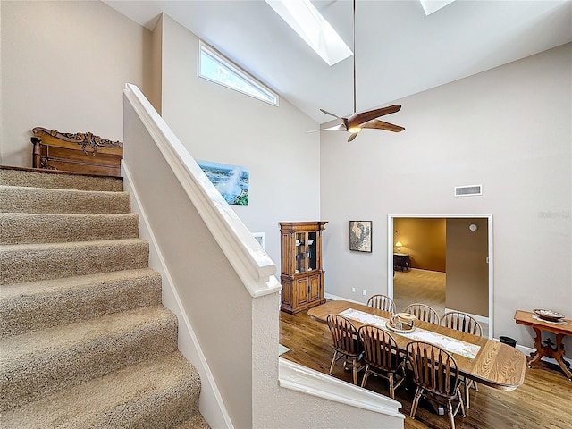 staircase with ceiling fan, high vaulted ceiling, a skylight, and hardwood / wood-style flooring