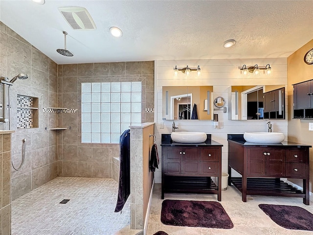 bathroom featuring a tile shower, tile walls, a textured ceiling, and vanity