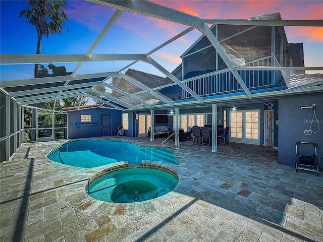 pool at dusk featuring a lanai, ceiling fan, an in ground hot tub, and a patio area