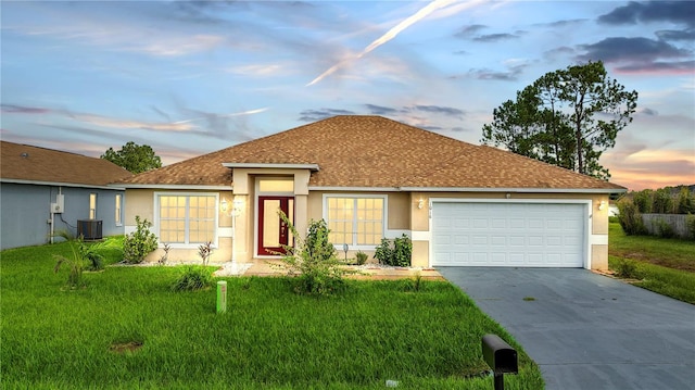 ranch-style house featuring a yard, a garage, and central AC unit