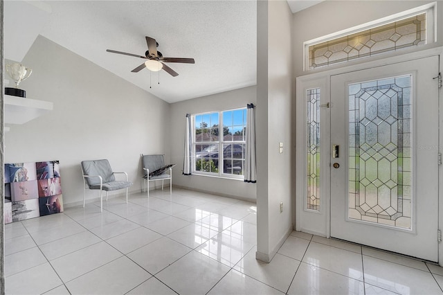 foyer entrance with a textured ceiling, ceiling fan, light tile patterned floors, and vaulted ceiling