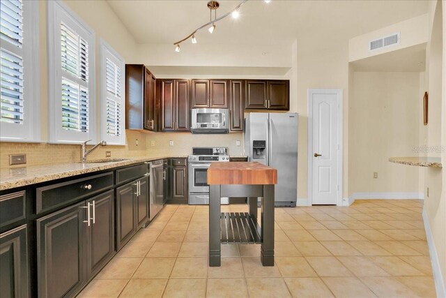 kitchen featuring light tile patterned floors, appliances with stainless steel finishes, light stone counters, and sink