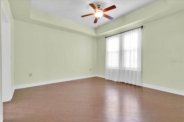 empty room with ceiling fan, a raised ceiling, and dark hardwood / wood-style flooring