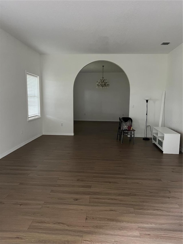 empty room with dark wood-type flooring and a notable chandelier