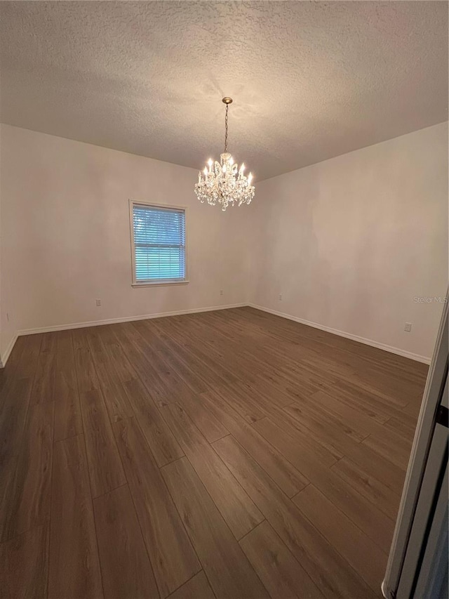 empty room with an inviting chandelier, dark hardwood / wood-style flooring, and a textured ceiling