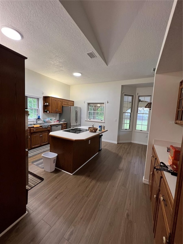 kitchen with a textured ceiling, a center island, stainless steel appliances, and dark wood-type flooring