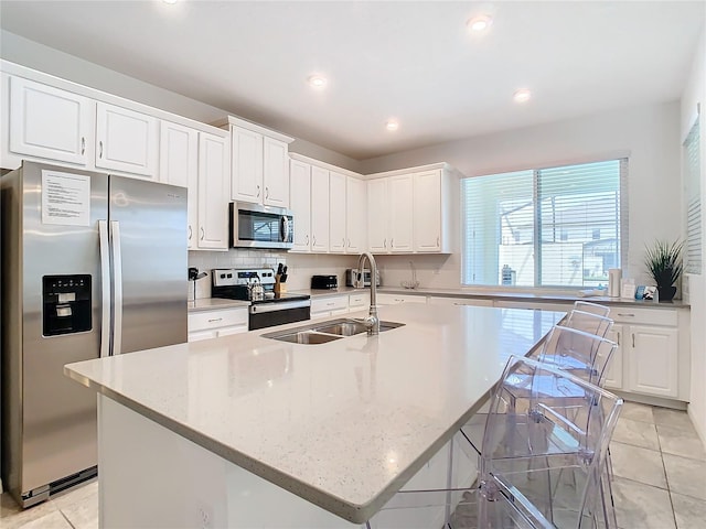 kitchen featuring an island with sink, light stone countertops, appliances with stainless steel finishes, and white cabinets