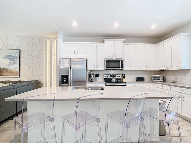 kitchen with white cabinets, appliances with stainless steel finishes, a large island with sink, and sink