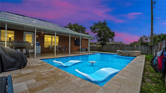 pool at dusk with a patio area and an in ground hot tub