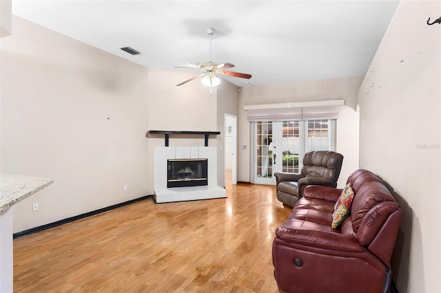 living room featuring light hardwood / wood-style flooring, ceiling fan, a tile fireplace, and french doors