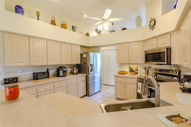 kitchen featuring light tile patterned floors, appliances with stainless steel finishes, sink, ceiling fan, and a towering ceiling