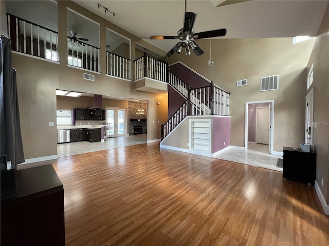 unfurnished living room featuring a towering ceiling, ceiling fan, and light hardwood / wood-style floors