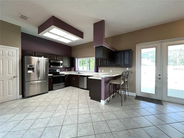 kitchen featuring a kitchen bar, stainless steel appliances, kitchen peninsula, and light tile patterned flooring