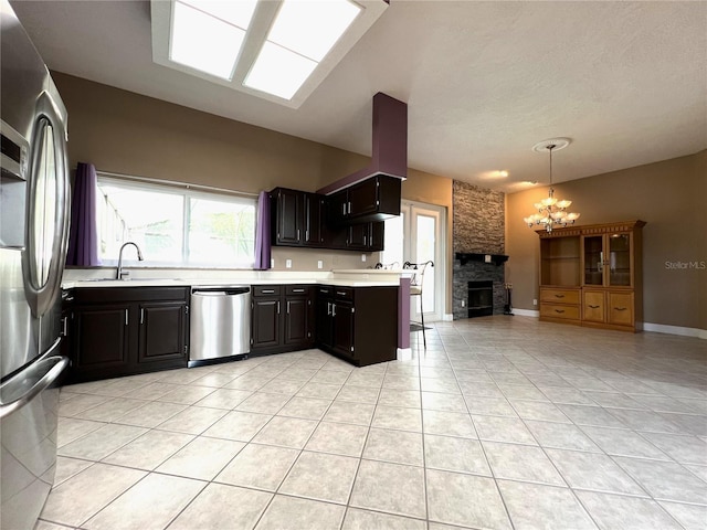 kitchen featuring a fireplace, a notable chandelier, stainless steel appliances, sink, and light tile patterned flooring