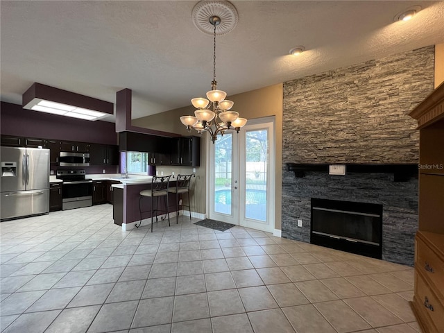 kitchen with a breakfast bar area, a stone fireplace, appliances with stainless steel finishes, kitchen peninsula, and a chandelier