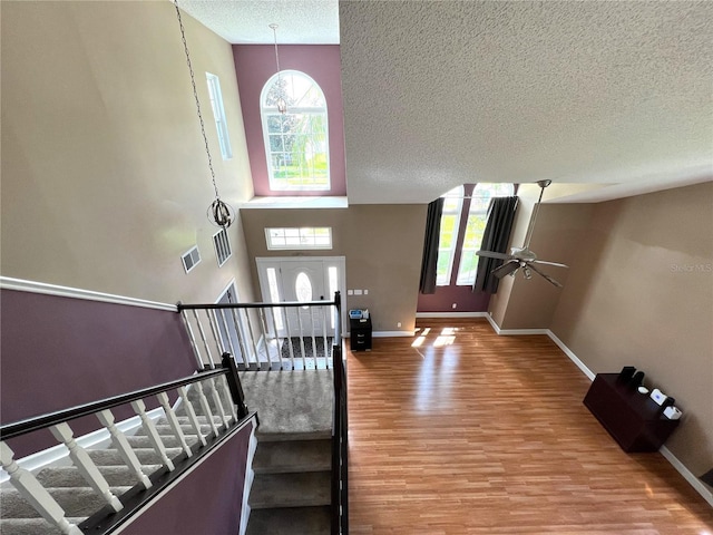 staircase featuring a high ceiling, ceiling fan, hardwood / wood-style flooring, and a textured ceiling