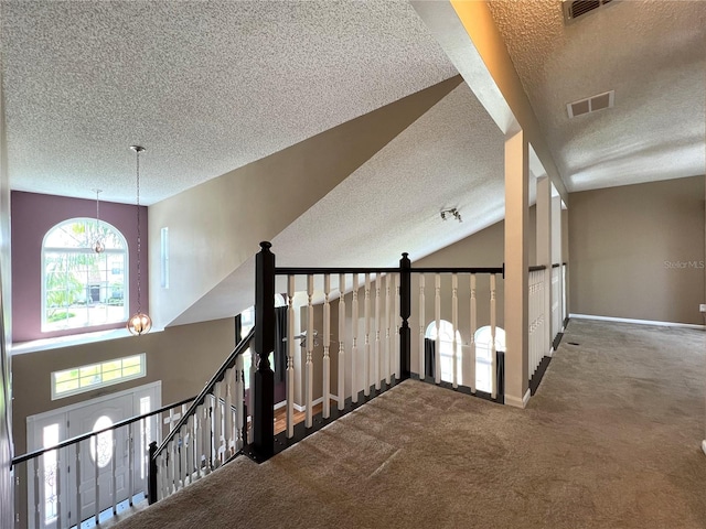 hall with a textured ceiling, vaulted ceiling, an inviting chandelier, and carpet floors