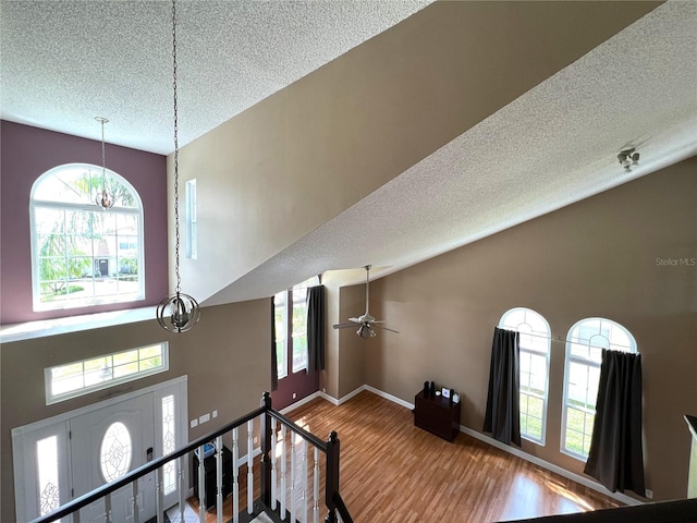 stairway with ceiling fan with notable chandelier, a textured ceiling, hardwood / wood-style flooring, and a high ceiling