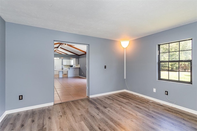 spare room with light hardwood / wood-style floors, lofted ceiling, and a textured ceiling