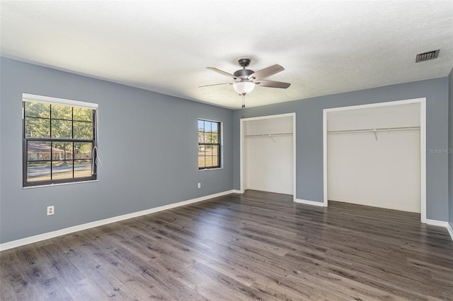 unfurnished bedroom with a textured ceiling, multiple closets, ceiling fan, and dark hardwood / wood-style floors