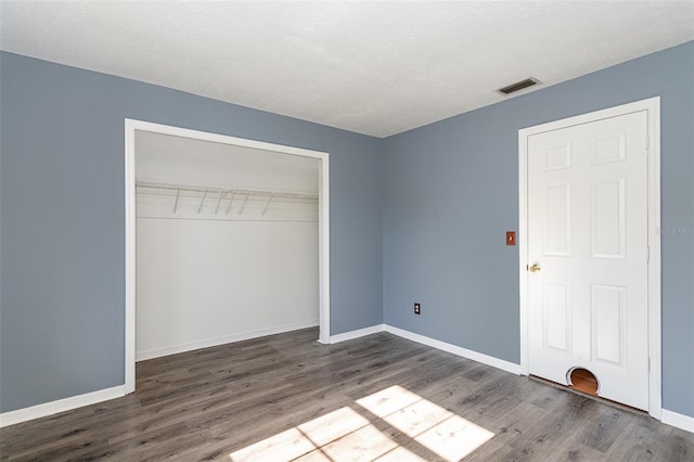 unfurnished bedroom with a textured ceiling, dark hardwood / wood-style floors, and a closet