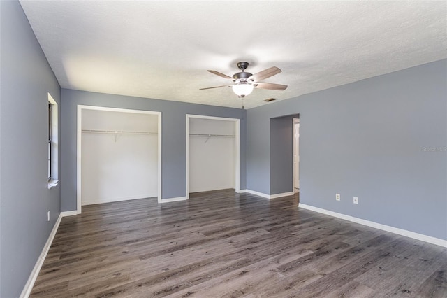 unfurnished bedroom featuring a textured ceiling, ceiling fan, dark wood-type flooring, and multiple closets