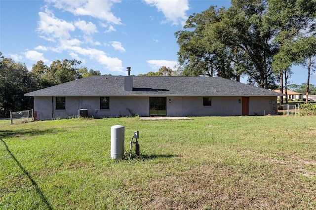 rear view of property featuring central air condition unit and a lawn