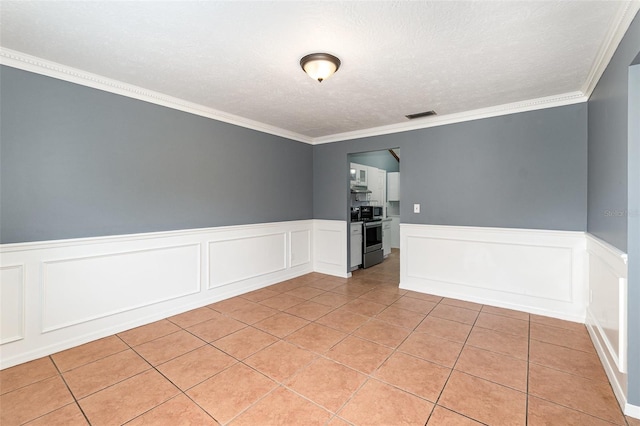 spare room featuring light tile patterned floors, visible vents, wainscoting, and a textured ceiling